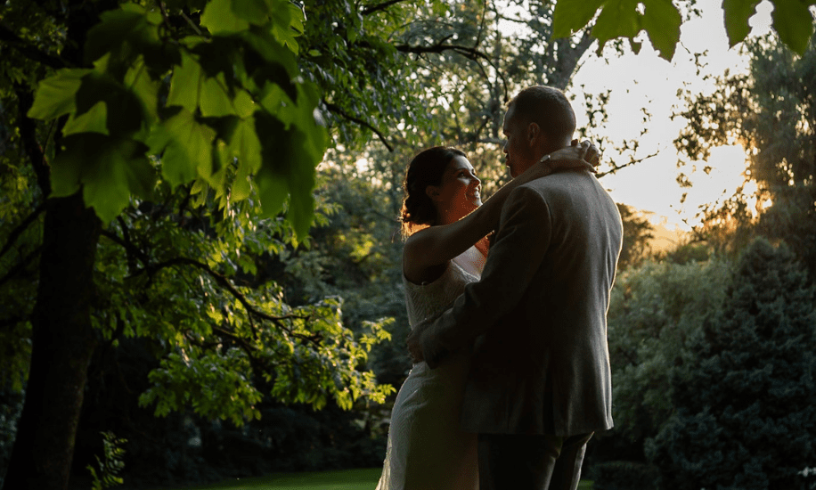 Bride and groom embracing during sunset in a lush, green countryside garden, surrounded by trees, at their wedding venue.