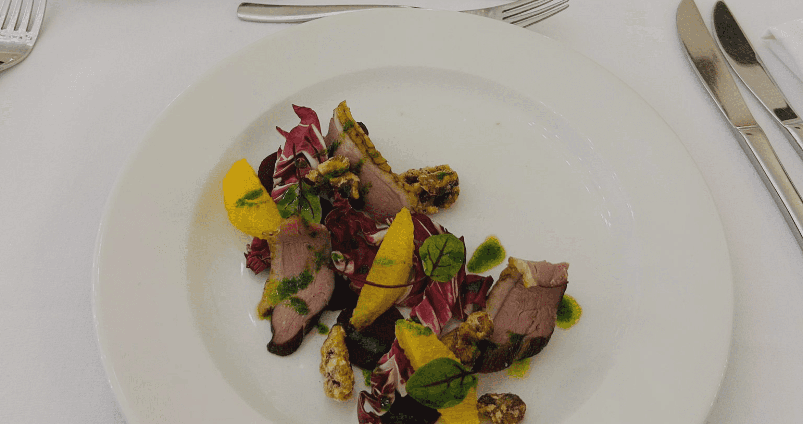 Duck starter with orange segments, crystalised walnuts and micro salad on a white plate, served on a dining table