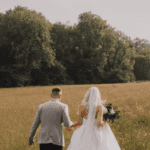 Bride and groom walking hand-in-hand through a grassy field near our wedding venue, surrounded by natural countryside beauty.