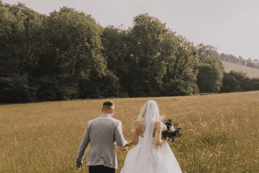 Bride and groom walking hand-in-hand through a grassy field near our wedding venue, surrounded by natural countryside beauty.