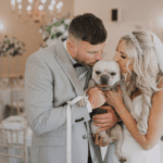 Bride and groom posing with their beloved dog on their wedding day, capturing a heartwarming moment of love and joy.