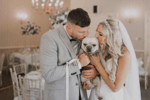 Bride and groom posing with their beloved dog on their wedding day, capturing a heartwarming moment of love and joy.